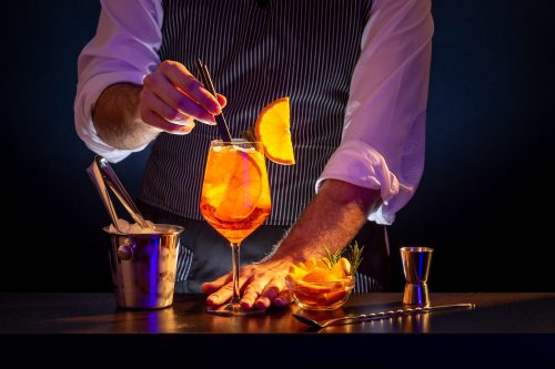 Bartender adding drinking straws into Aperol spritz cocktail glass